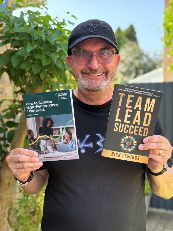 Man with glasses wearing black cap holding up two books
